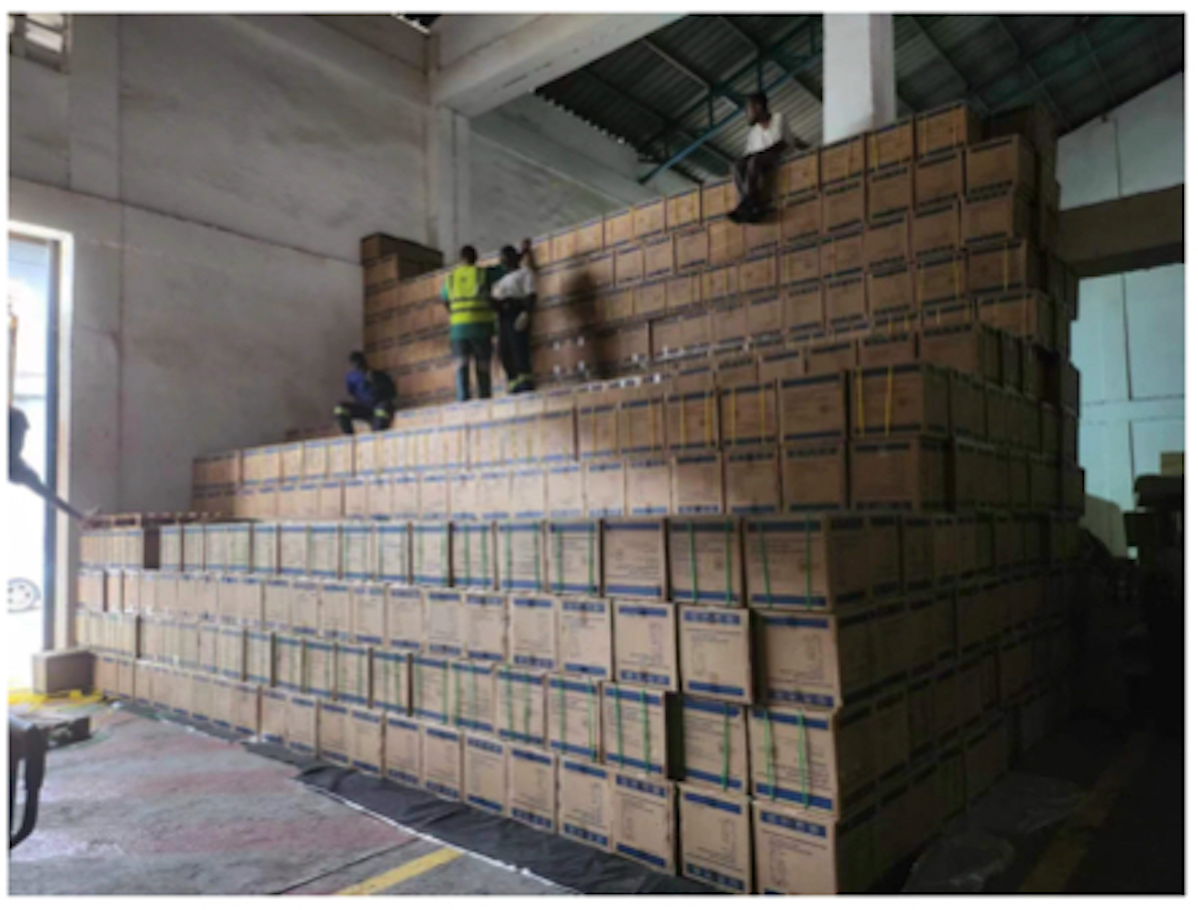 Packed cartons stacked inside a warehouse, with workers beside the shipment.